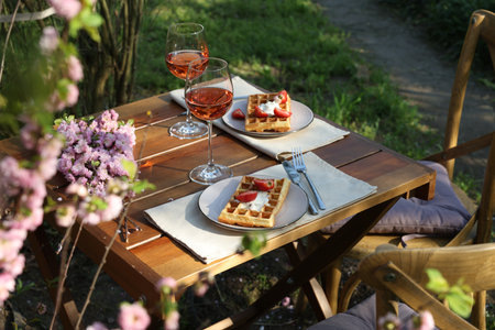 Delicious Belgian waffles with fresh strawberries and wine served on table in spring gardenの写真素材
