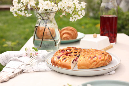 Stylish table setting with beautiful spring flowers, fruit drink and pie in garden