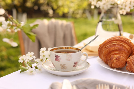 Stylish table setting with beautiful spring flowers, tea and croissants in garden