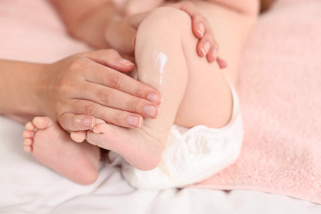 Woman applying body cream onto baby`s skin on bed, closeupの写真素材