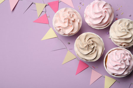 Delicious birthday cupcakes, sprinkles and bunting flags on violet background, flat lay. Space for textの写真素材