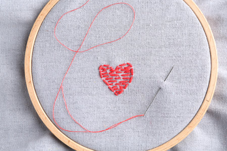 Embroidered red heart and needle on gray cloth, top viewの写真素材