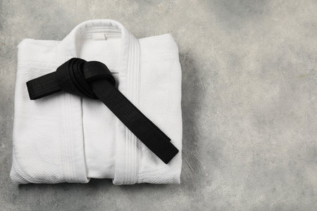 Black karate belt and white kimono on gray textured background, top view. Space for textの写真素材
