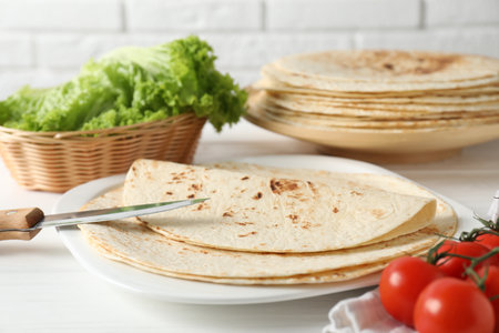 Tasty homemade tortillas, tomatoes, lettuce and knife on white wooden table