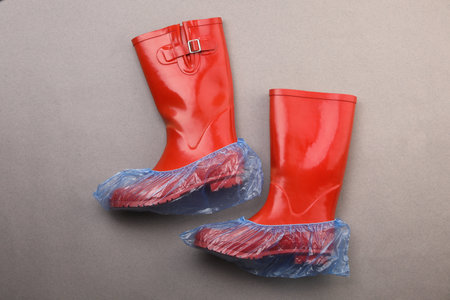Rubber boots in shoe covers on gray background, top view
