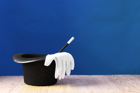 Magician's hat, wand and gloves on wooden table against blue background, space for textの写真素材
