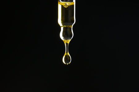 Dripping tincture from pipette on black background, closeup