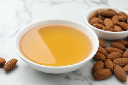 Almond oil in bowl and nuts on white marble table, closeupの写真素材