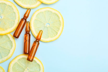 Skincare ampoules with vitamin C and slices of lemon on light blue background, flat lay. Space for textの写真素材