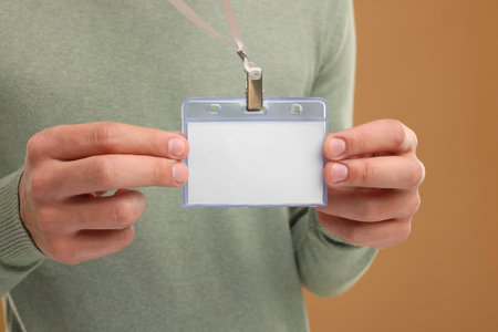 Man with blank badge on light brown background, closeup