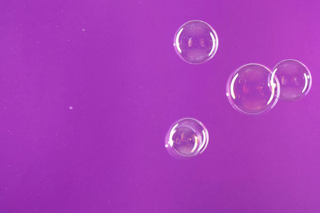 Beautiful transparent soap bubbles on violet background, space for textの写真素材