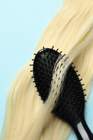 Stylish brush with blonde hair strand on light blue background, top view