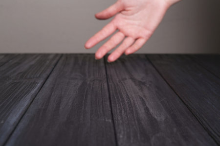 Woman holding hand above black wooden table, selective focus. Space for textの写真素材