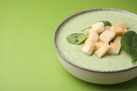 Delicious spinach cream soup with leaves and croutons in bowl on green background, space for textの写真素材