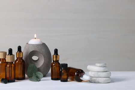 Different aromatherapy products, burning candle and eucalyptus leaves on white wooden table against light background, space for textの写真素材