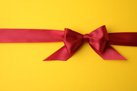 Red satin ribbon with bow on yellow background, top viewの写真素材
