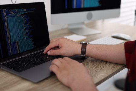 Programmer working with laptop at desk in office, closeup