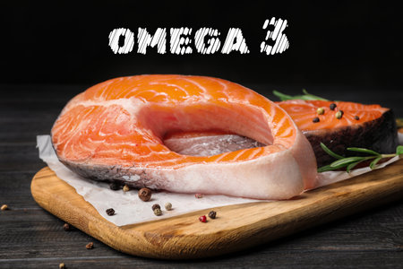 Omega 3. Board with fresh salmon steaks and peppercorns on black wooden table, closeupの写真素材