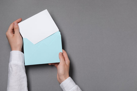 Woman taking card out of letter envelope at gray table, top view. Space for textの写真素材