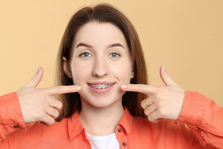 Portrait of smiling woman pointing at her dental braces on beige backgroundの写真素材