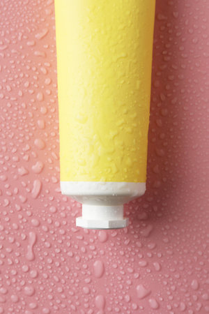 Moisturizing cream in tube on pink background with water drops, top view