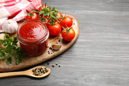Tasty ketchup, fresh tomatoes, parsley and spices on gray wooden table, space for textの写真素材