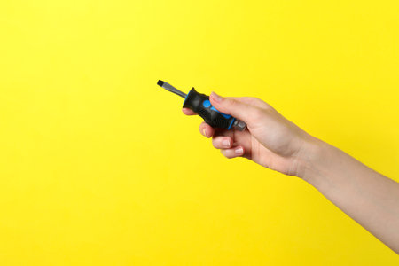 Woman holding small screwdriver on yellow background, closeup. Space for textの写真素材