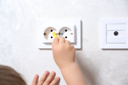 Little child playing with toy screwdriver and electrical socket at home, closeup. Dangerous situationの写真素材