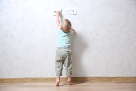 Little child playing with electrical socket indoors, back view. Dangerous situationの写真素材