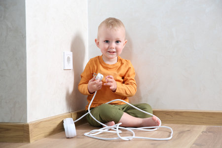 Little child playing with power strip plug near electrical socket at home. Dangerous situationの写真素材