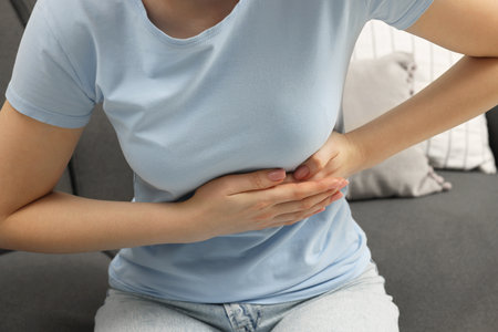 Woman suffering from stomach pain on sofa indoors, closeupの写真素材