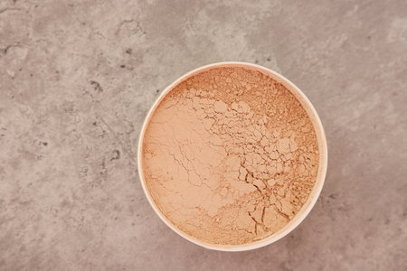 Face powder on gray textured table, top view. Space for text