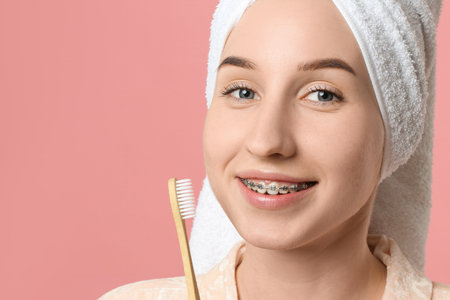 Portrait of smiling woman with dental braces and toothbrush on pink background, closeup. Space for textの写真素材