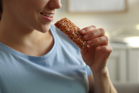Woman eating tasty granola bar at home, closeupの写真素材