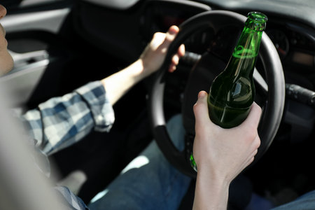 Man with bottle of beer driving car, closeup. Don't drink and drive conceptの写真素材