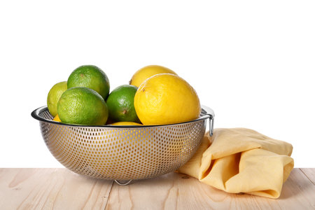 Fresh fruits in colander and napkin on wooden table against white backgroundの写真素材