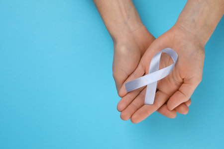 International Psoriasis Day. Woman with light blue ribbon as symbol of support on light blue...