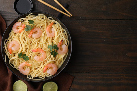 Tasty spaghetti with shrimps, parsley, lime and soy sauce on wooden table, flat lay. Space for textの写真素材