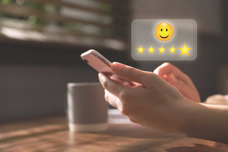 Woman leaving service feedback with smartphone at home, closeup. Stars and emoticon over deviceの写真素材