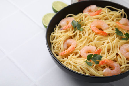 Tasty spaghetti with shrimps and parsley in bowl on light tiled table, closeup. Space for textの写真素材