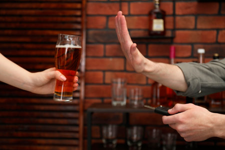 Man with car keys refusing from alcohol while woman offering him beer in bar, closeup. Don't drink and drive conceptの写真素材