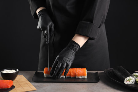Chef in gloves cutting sushi roll at gray table, closeupの写真素材