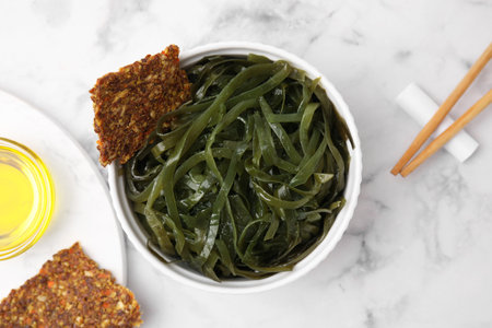 Tasty seaweed salad in bowl served on white marble table, flat lay