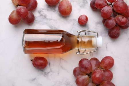 Wine vinegar in glass bottle and grapes on white marble table, flat lay