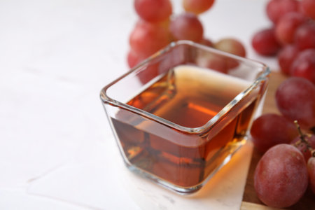 Wine vinegar in glass bowl and grapes on white table, closeup. Space for textの写真素材