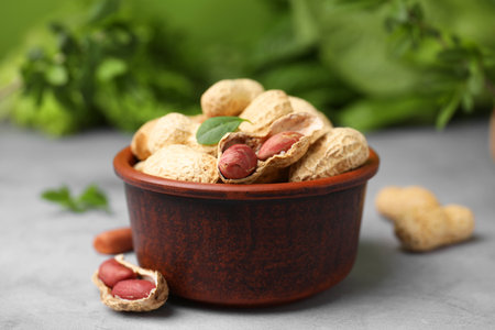 Fresh unpeeled peanuts in bowl on gray table against blurred green background, closeup