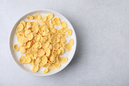 Breakfast cereal. Corn flakes and milk in bowl on light gray table, top view. Space for textの写真素材