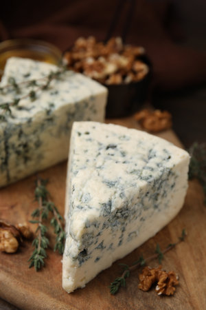 Tasty blue cheese with thyme and walnuts on wooden table, closeup