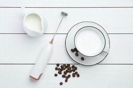Flat lay composition with mini mixer (milk frother), whipped milk and coffee beans on white wooden tableの写真素材