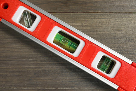 Red building level on wooden table, top view